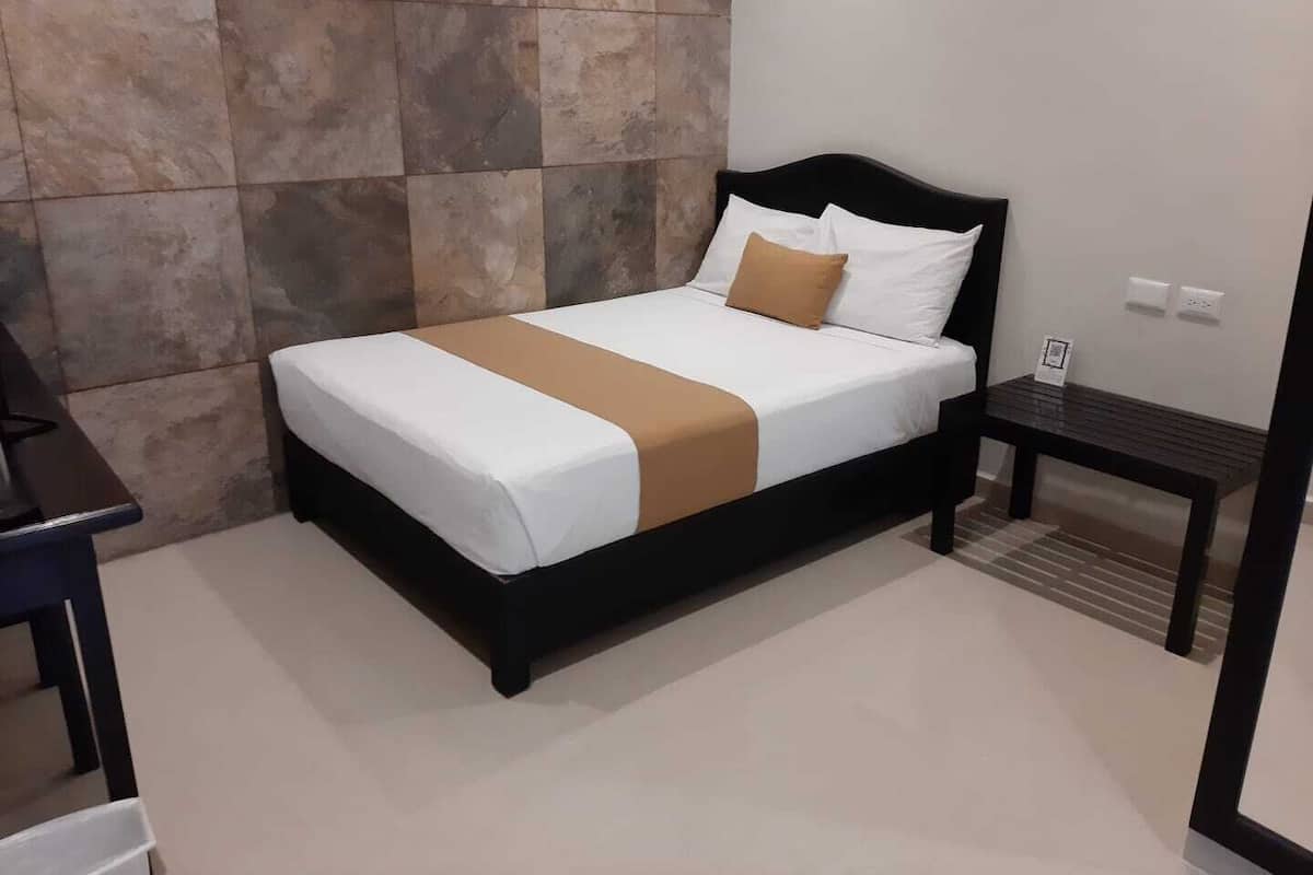 A neatly made bed with a white and brown bedspread, a black headboard, and a small bedside table with a lamp.