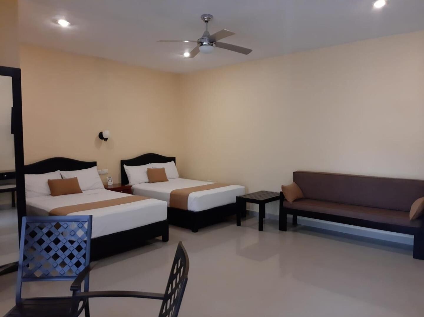 A hotel room with two beds, a sofa, a small table, and a ceiling fan.