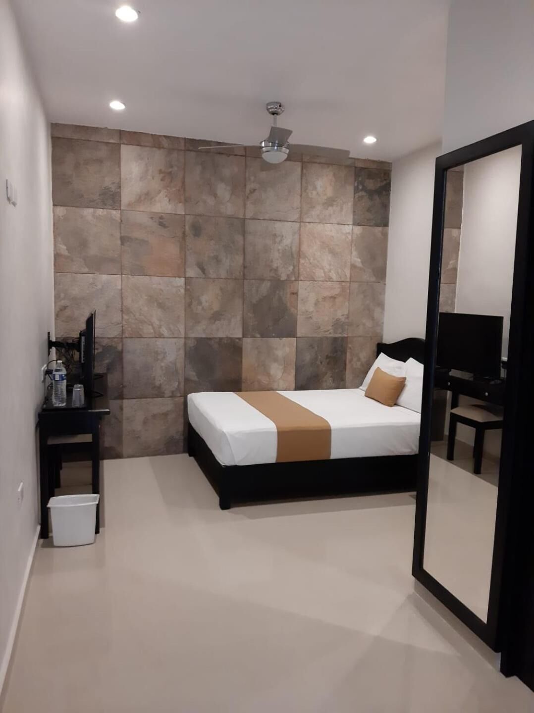 Un dormitorio con cama, mesita de noche, espejo y ventilador de techo.