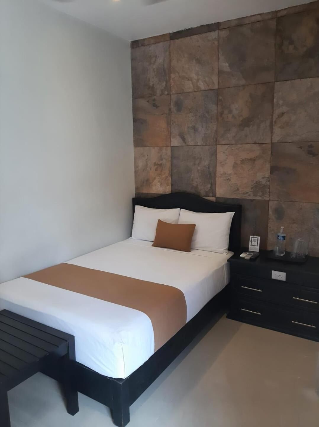 A hotel room with a bed, bedside tables, and a wall with a stone-like pattern.
