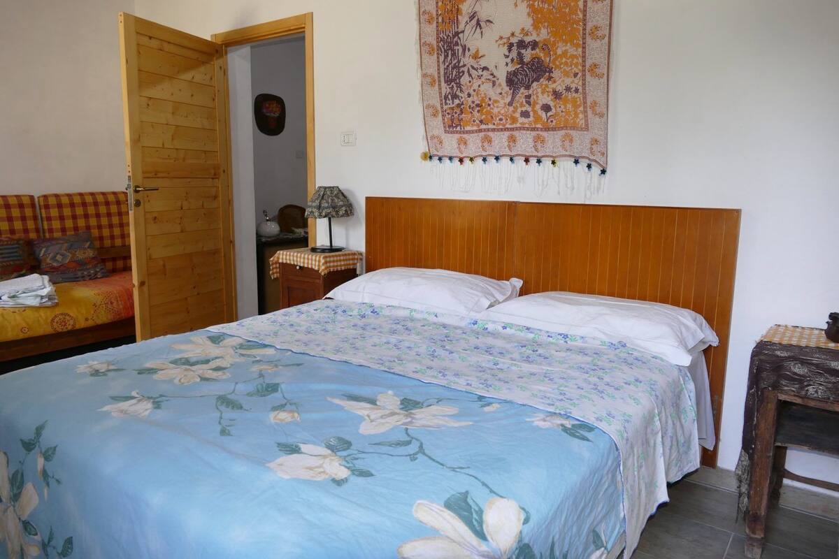 Une chambre avec un lit doté d’une tête de lit en bois, un canapé à carreaux et une tapisserie au mur.