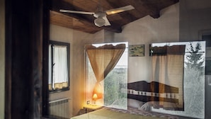 A bedroom with a bed, a nightstand, a lamp, a ceiling fan, and a window with a view of trees.