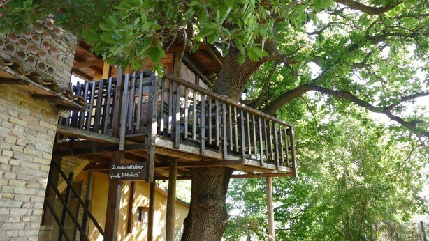 A treehouse with a wooden balcony, a brick wall, and a sign in a foreign language.