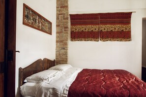 Un dormitorio con cama de madera, ropa de cama blanca, pared de ladrillo y un tapiz.