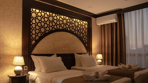 A hotel room with two beds, a decorative headboard, bedside lamps, and a view of the city through large windows. - Orient Star Varaxsha (Bukhara)