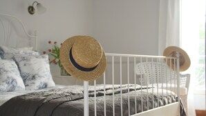 Een bed met een grijze deken, een wit metalen wieg en een strohoed op de wieg.