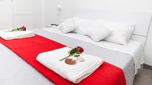 A hotel room with a bed, white bedding, a red blanket, a rose, seashells, and a white door. - Orlando Bay View (Balestrate)