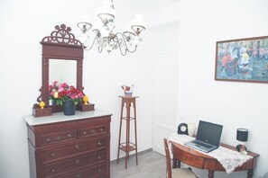Ein Zimmer mit einem hölzernen Schminktisch, einem Laptop auf einem Tisch, einer Chandelüster und einem gerahmten Bild an der Wand.