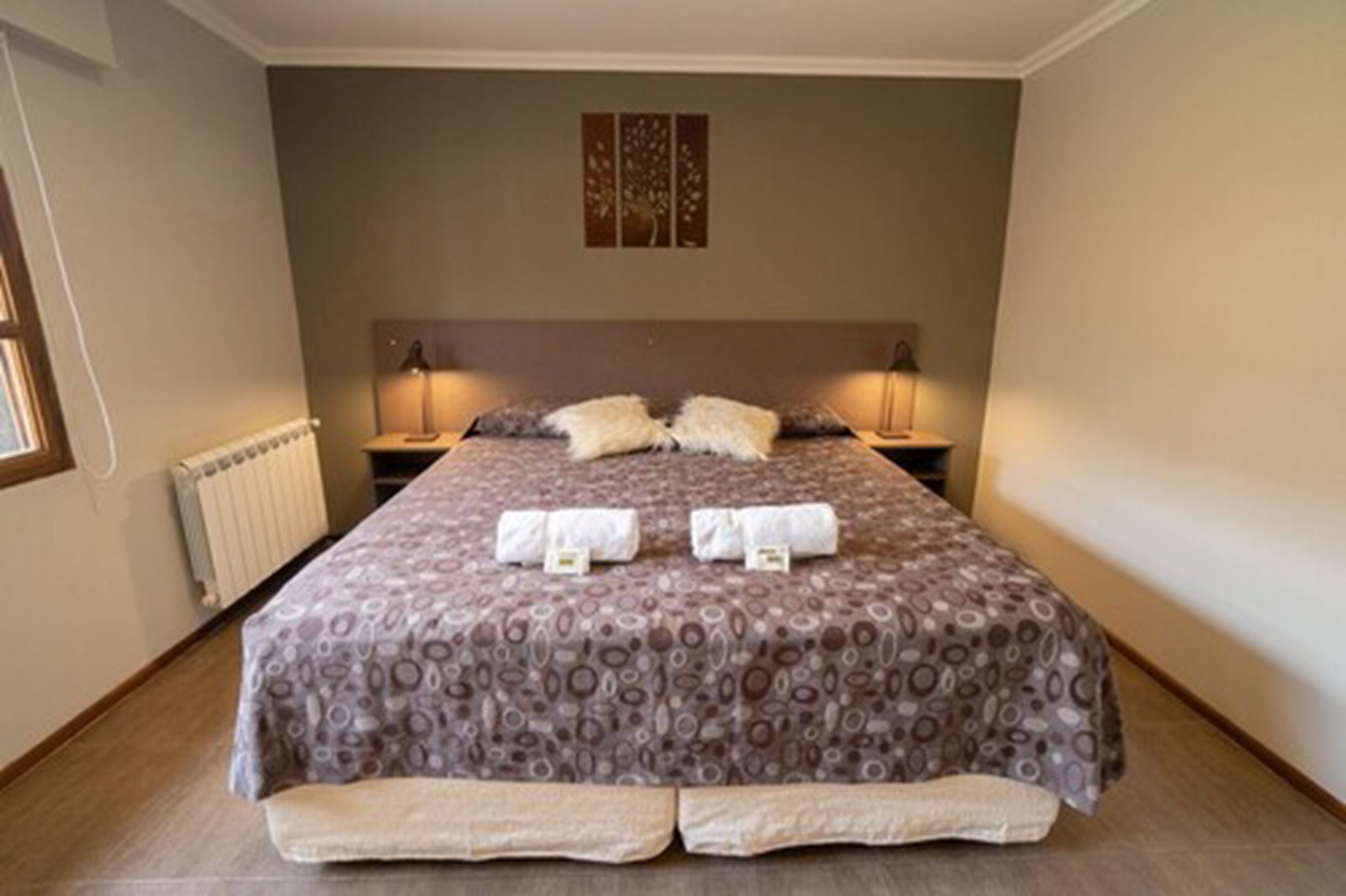 A neatly made bed with a patterned bedspread, two pillows, and two rolled towels on the bed.
