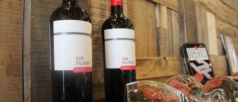 Two bottles of wine with labels, a glass, and a smartphone on a wooden surface.