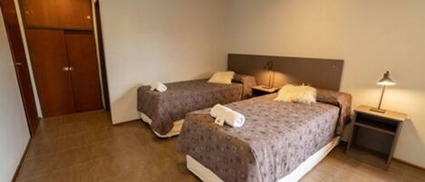 A hotel room with two beds, a wardrobe, a bedside table with a lamp, and a nightstand.