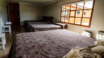 Une chambre d’hôtel avec deux lits, un bureau et une fenêtre donnant sur des bâtiments en bois.