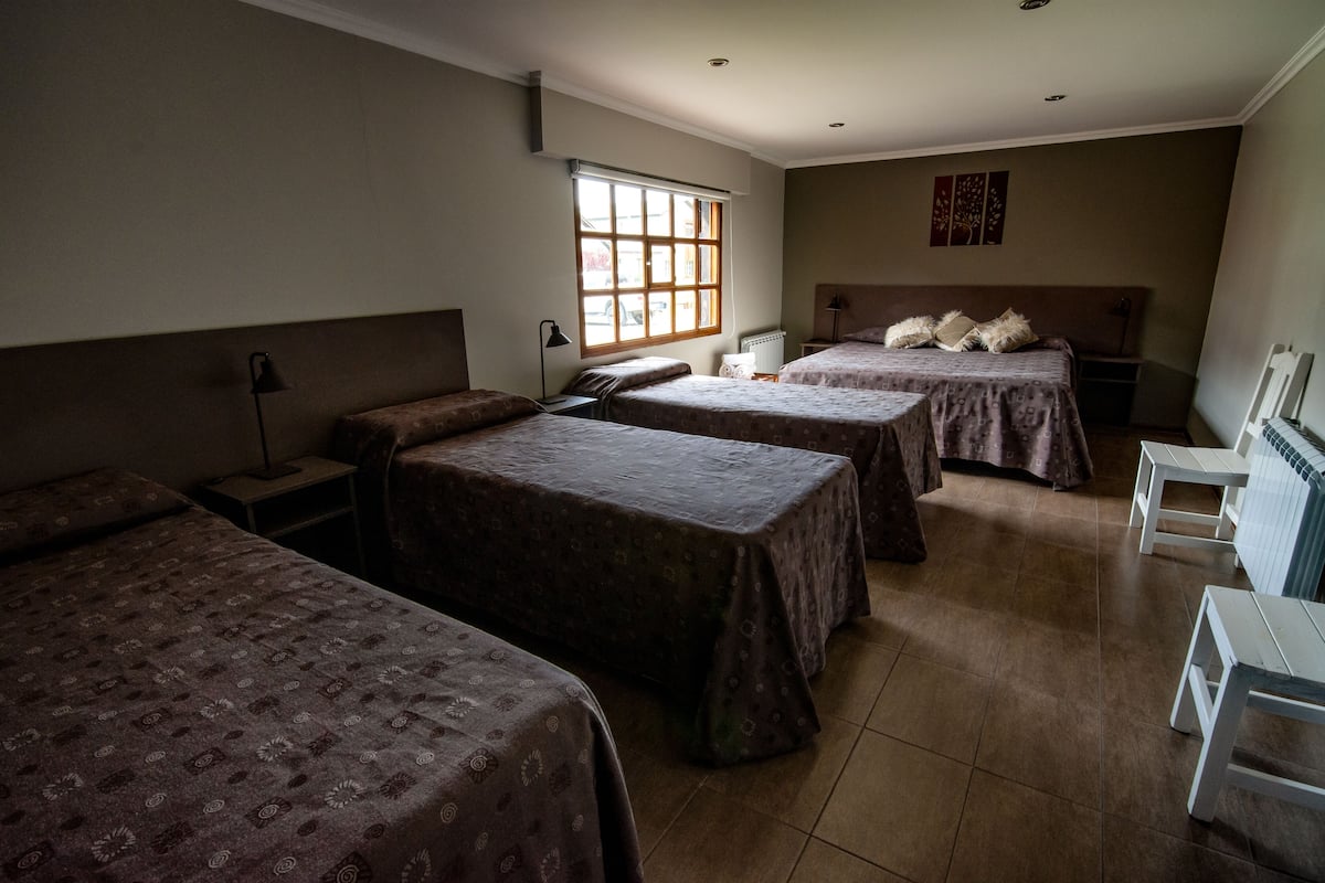 Une chambre de dortoir avec trois lits simples, une petite table, une chaise et un radiateur.