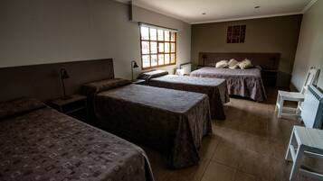 A dormitory room with three single beds, a small table, a chair, and a radiator.