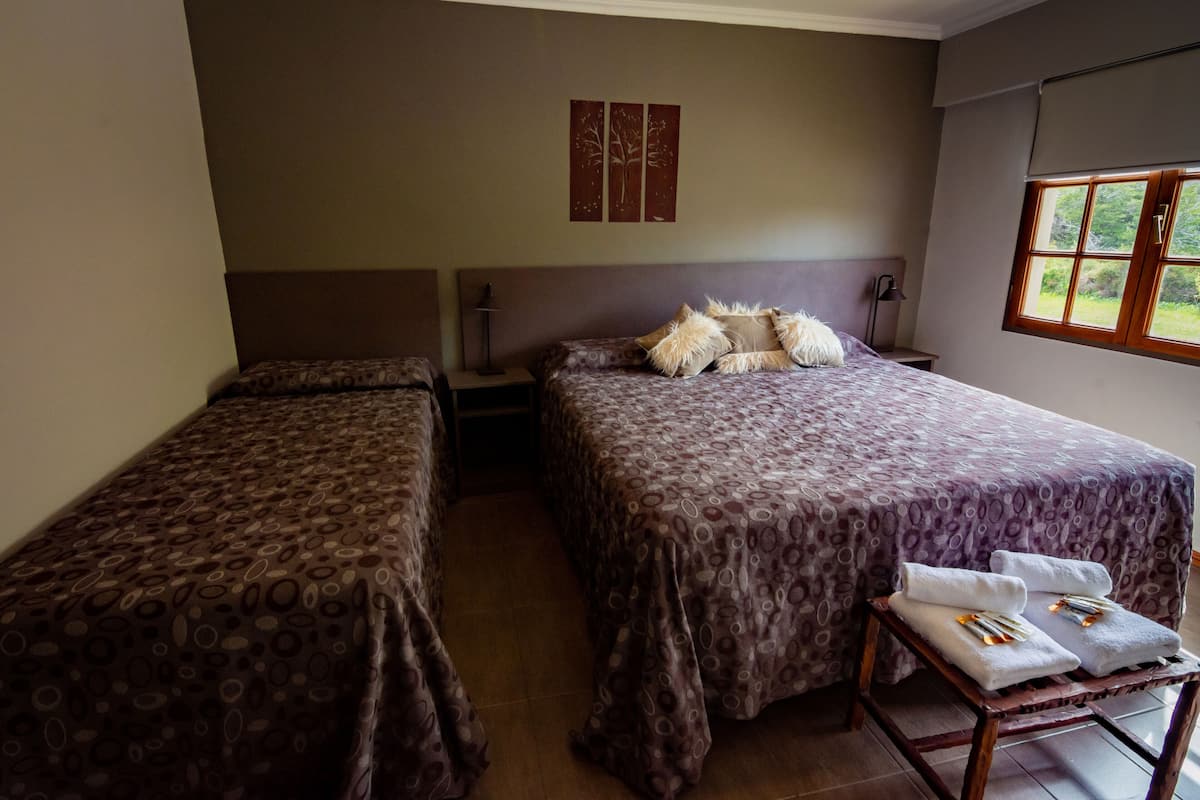Une chambre avec deux lits, une petite table avec des serviettes, une lampe et une fenêtre donnant sur un paysage verdoyant.