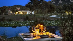 A dining table set with glasses, a candle, and a bowl by a lake at dusk. - Li Neuli Country Club (Arzachena)