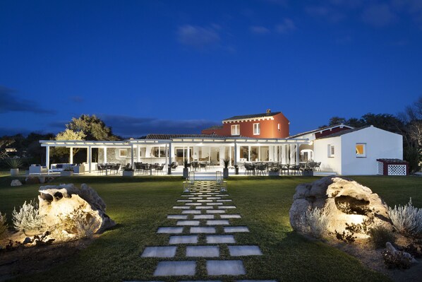 A modern house with a covered patio, stone pathway, and large rocks. - Li Neuli Country Club (Arzachena)