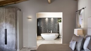 A modern bedroom with a large bed, a built-in bathtub, and a wooden ceiling. - Li Neuli Country Club (Arzachena)