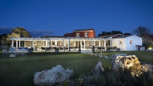 A large, modern building with a covered outdoor area, stone walls, and a well-maintained lawn. - Li Neuli Country Club (Arzachena)