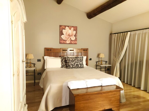 Une chambre à coucher bien aménagée, avec un grand lit, deux tables de chevet avec des lampes, un banc en bois et une œuvre d’art florale accrochée au mur.