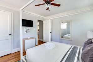 Ein Schlafzimmer mit einem Bett, einem Deckenventilator, einem an der Wand montierten Fernseher und einer Tür zu einem anderen Raum.