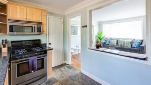 A kitchen with a stove, oven, microwave, and wooden cabinets. There is a window seat with a plant and cushions. - Light & Airy Family Home (Atlanta)