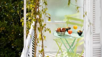 A balcony with a table set for breakfast, including croissants, a bowl of fruit, and a glass of orange juice.
