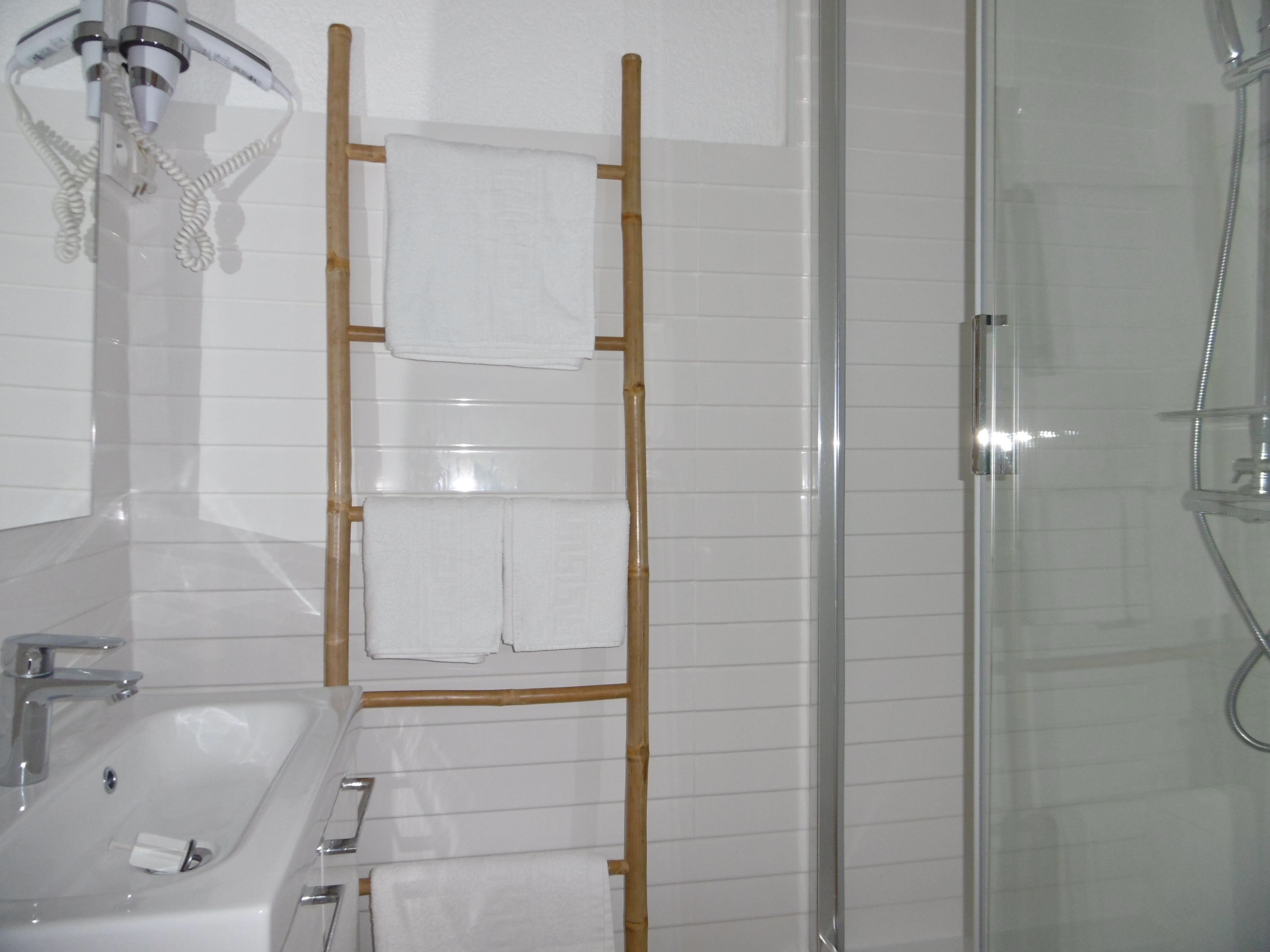 Une salle de bain avec une douche à parois de verre, un lavabo blanc avec un miroir et un porte-serviettes avec deux serviettes.
