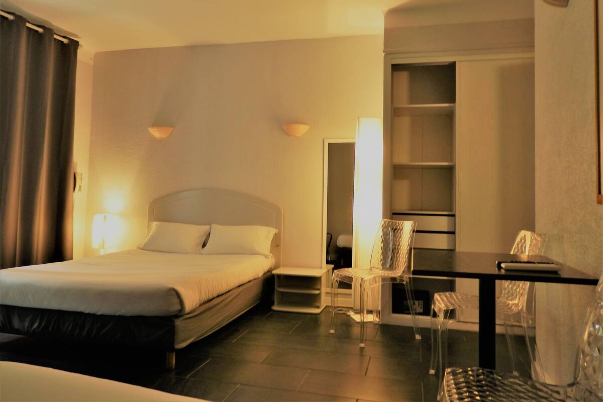 A hotel room with a bed, a desk, a chair, and a bookshelf.