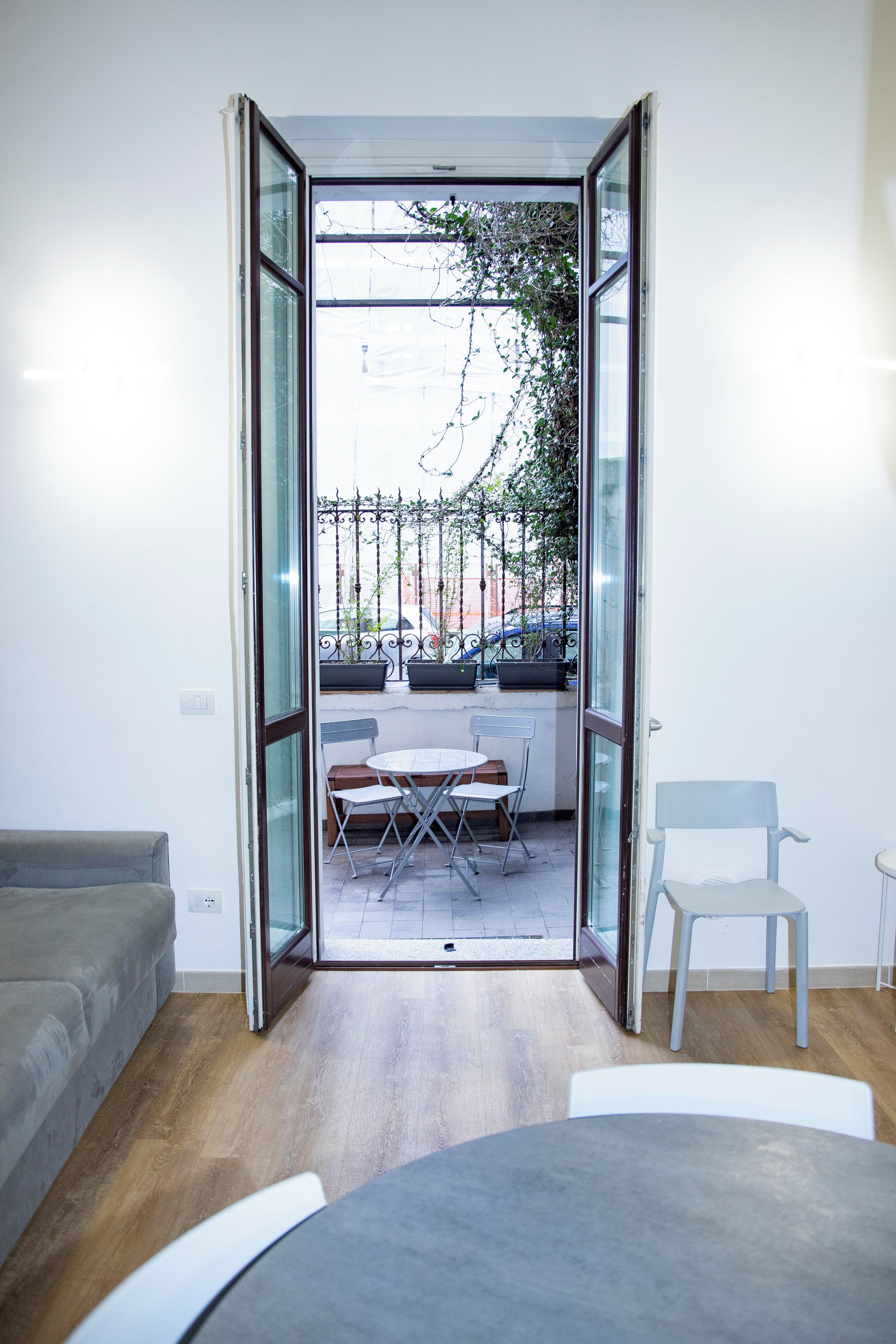 A room with a glass door leading to an outdoor area with a table and chairs, a sofa, and a chair.