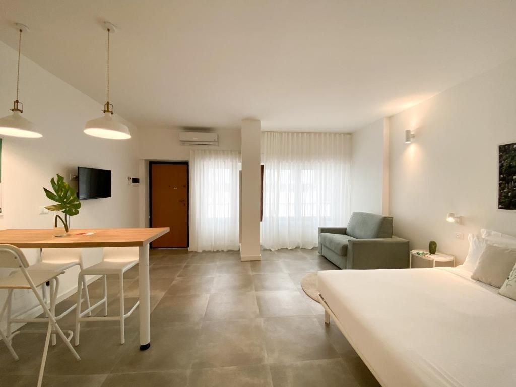 A modern hotel room with a bed, a desk with chairs, a sofa, and a television.