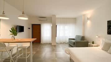 A modern hotel room with a bed, a desk with chairs, a sofa, and a television.