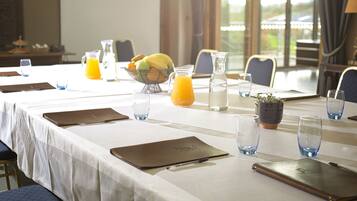 Un salón de conferencias con una larga mesa dispuesta para una reunión, equipado con carpetas, cuadernos y una jarra de jugo de naranja.