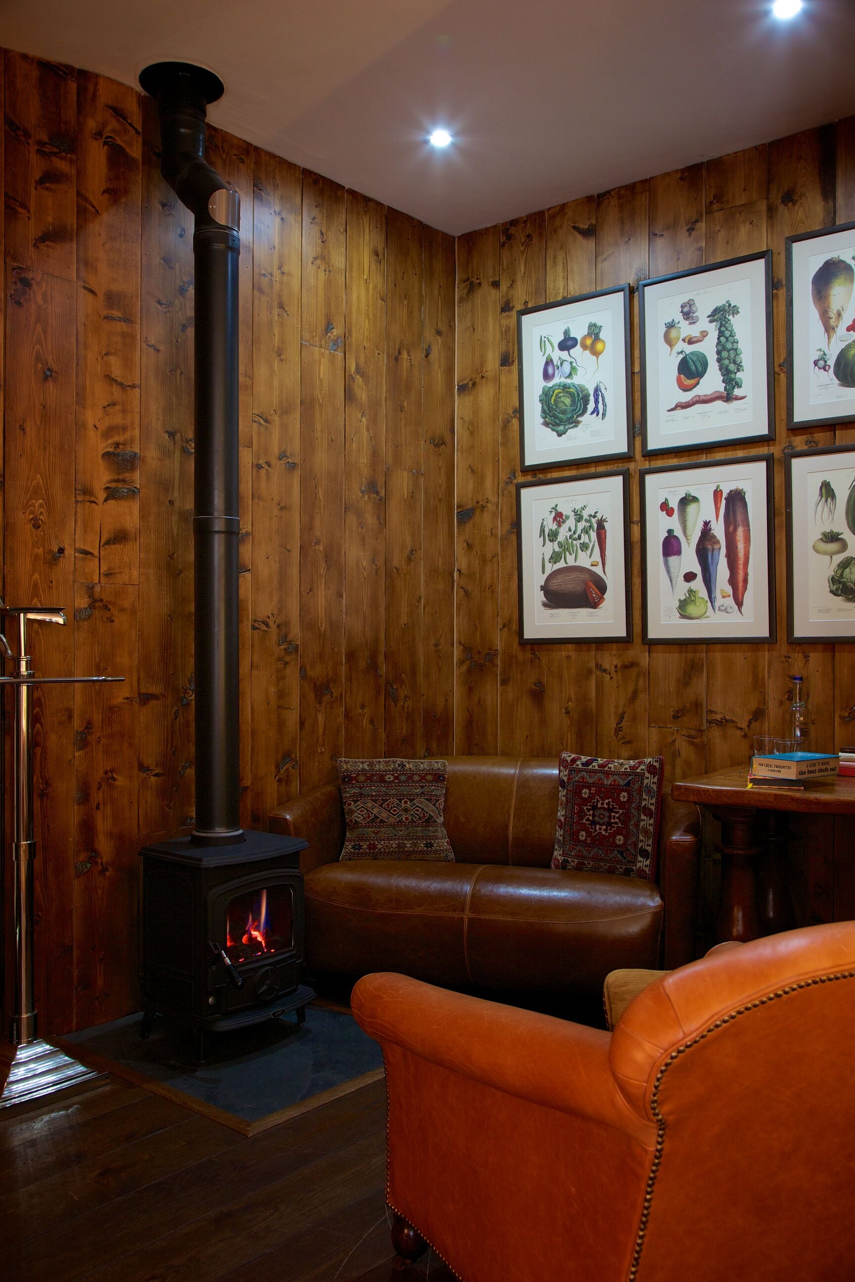 A cozy room with a wood-burning stove, a leather sofa, and framed botanical prints on the wall.