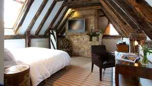 Un dormitorio acogedor en el ático con cama, una silla, un escritorio con lámpara, televisor y pared de piedra.