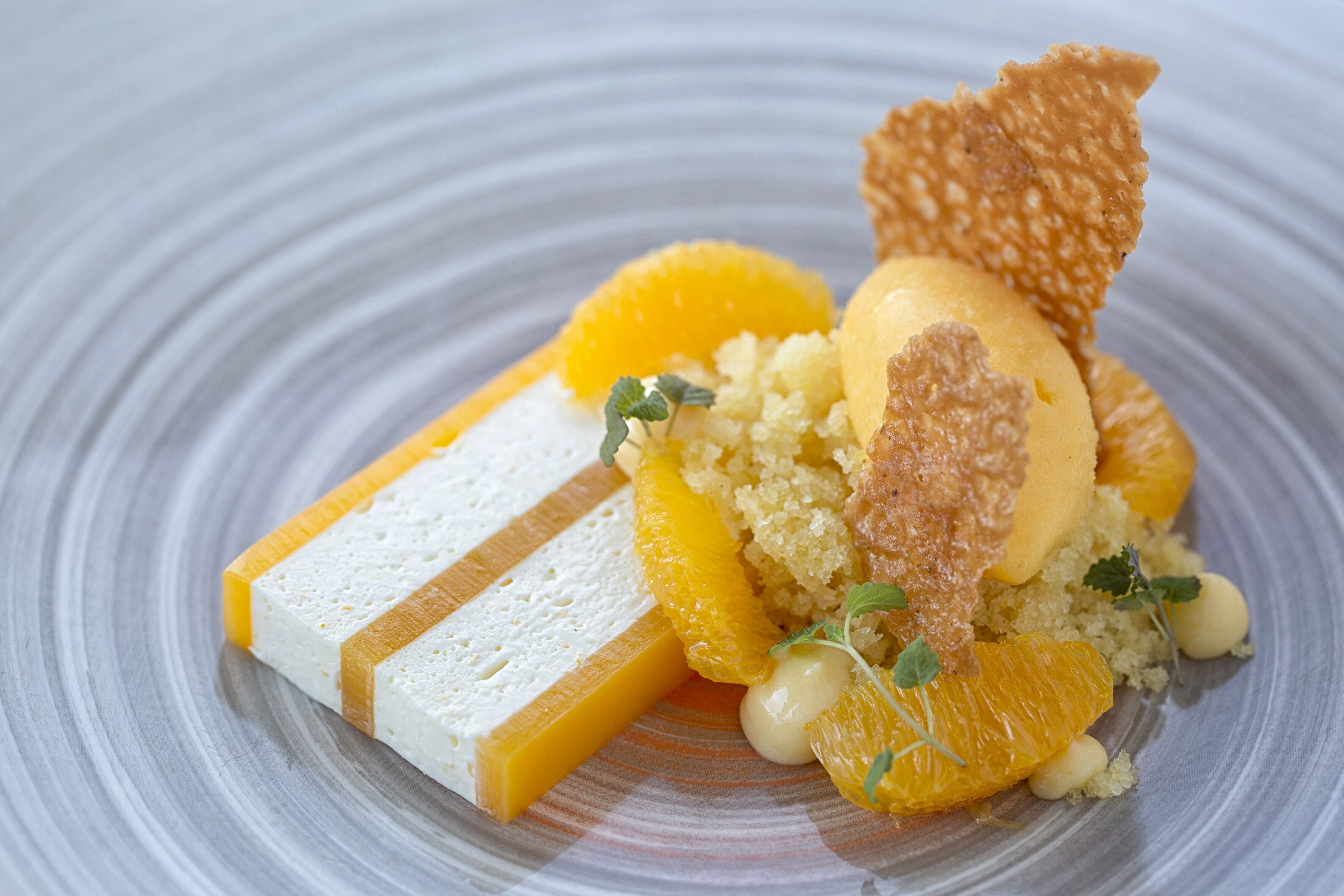 A dessert plate with a piece of white cake, orange segments, and a scoop of ice cream.