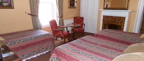 Ein Hotelzimmer mit zwei Betten, einem Sessel, einem kleinen Tisch, einem Kamin und einem Spiegel an der Wand.