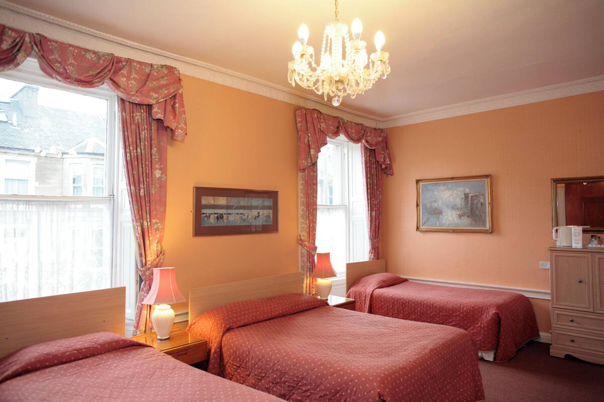 Habitación de hotel con dos camas, un candelabro, un cuadro y un aparador.