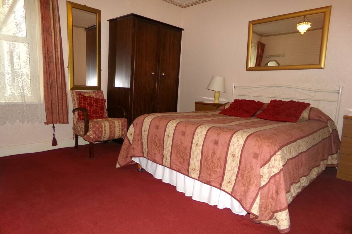 Un dormitorio con una cama grande, un armario de madera, una silla y un espejo en la pared.