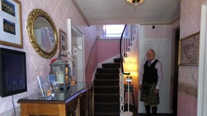 A hallway with a staircase, a wooden cabinet with glass doors, and a person in traditional attire. - Averon  Guest House (Edinburgh)