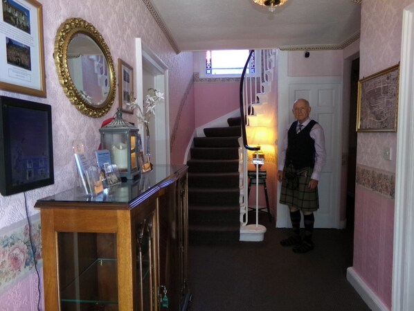 A hallway with a staircase, a wooden cabinet with glass doors, and a person in traditional attire. - Averon  Guest House (Edinburgh)