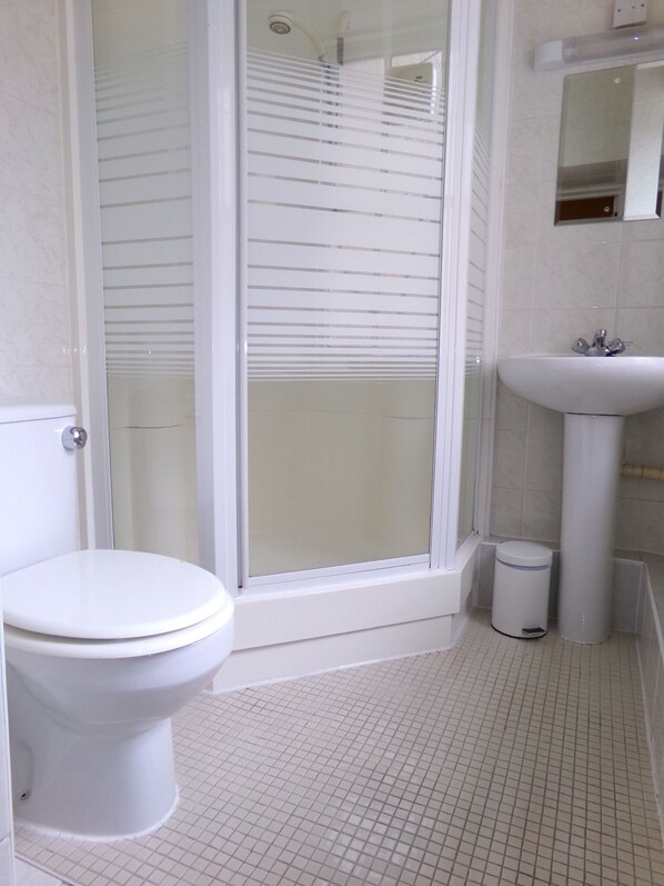 Un baño con inodoro, lavamanos y ducha con puertas de vidrio esmerilado.