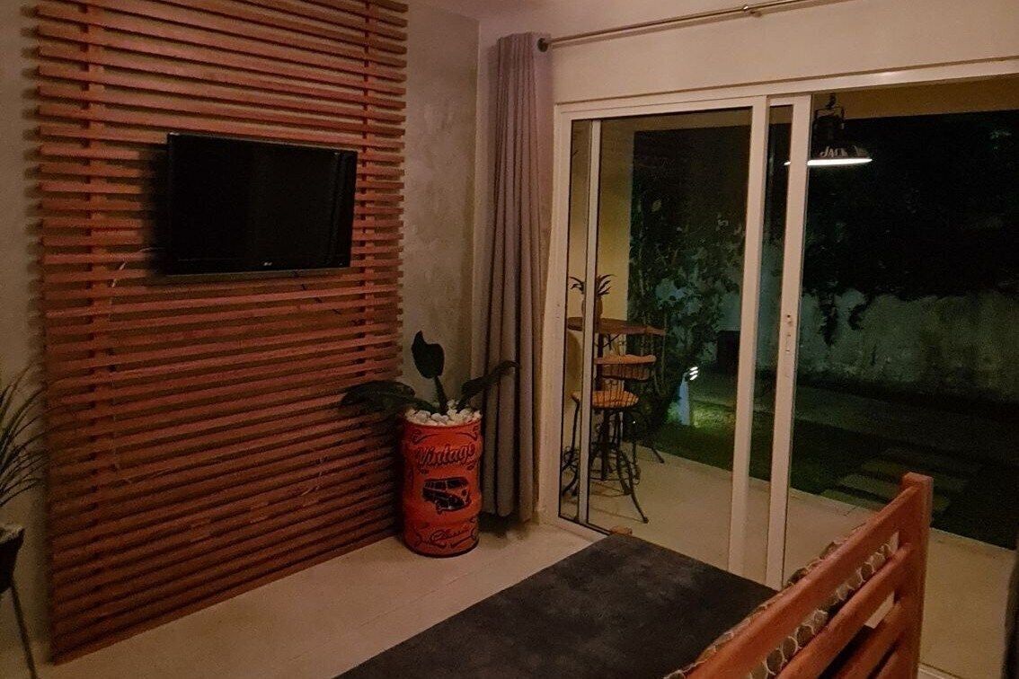 A room with a TV mounted on a wooden slatted wall, a sliding glass door leading to an outdoor area, and a red vintage-style planter.