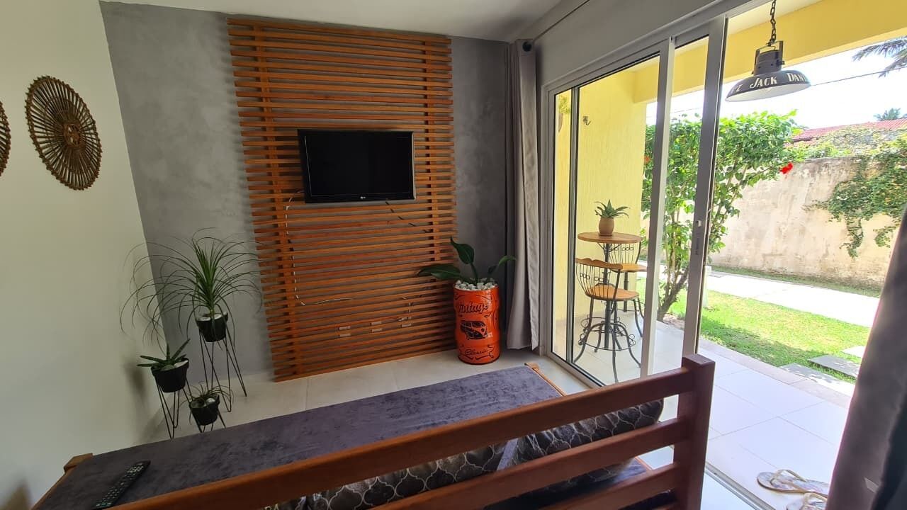 A balcony with a TV, potted plants, and a view of the garden.