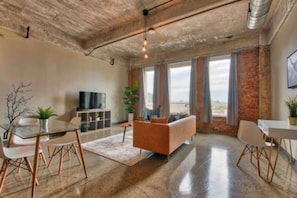 A spacious living area with a modern sofa, a glass dining table, and a television. - Downtown Luxury Lofts By RBA Living (Dallas)
