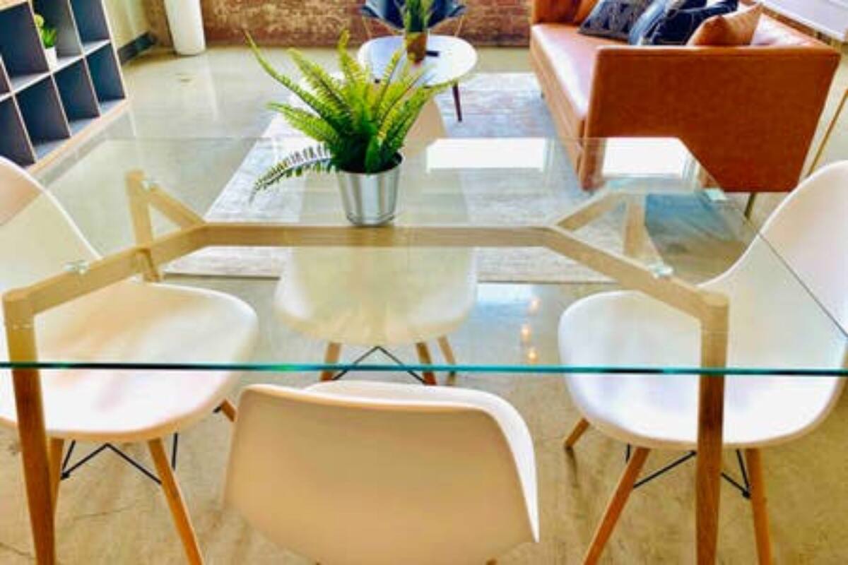 A modern living room with a glass coffee table, white chairs, a potted plant, and a sofa.