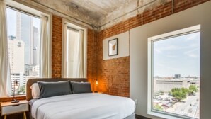 Un dormitorio con una ventana grande, una cama, una mesita de noche y vista a la ciudad.