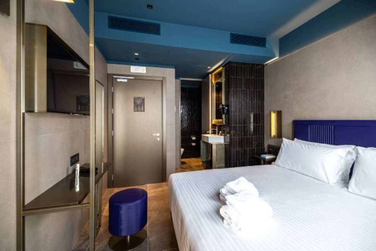 Habitación de hotel moderna con una cama grande, un escritorio y un baño visible a través de una puerta abierta.