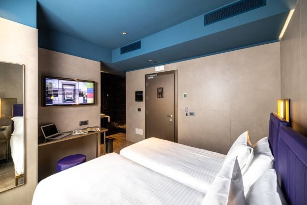 Habitación de hotel con cama, escritorio, laptop, televisión y puerta de baño.