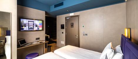 Ein Hotelzimmer mit einem Bett, einem Schreibtisch mit einem Laptop, einem Fernseher und einer Tür.